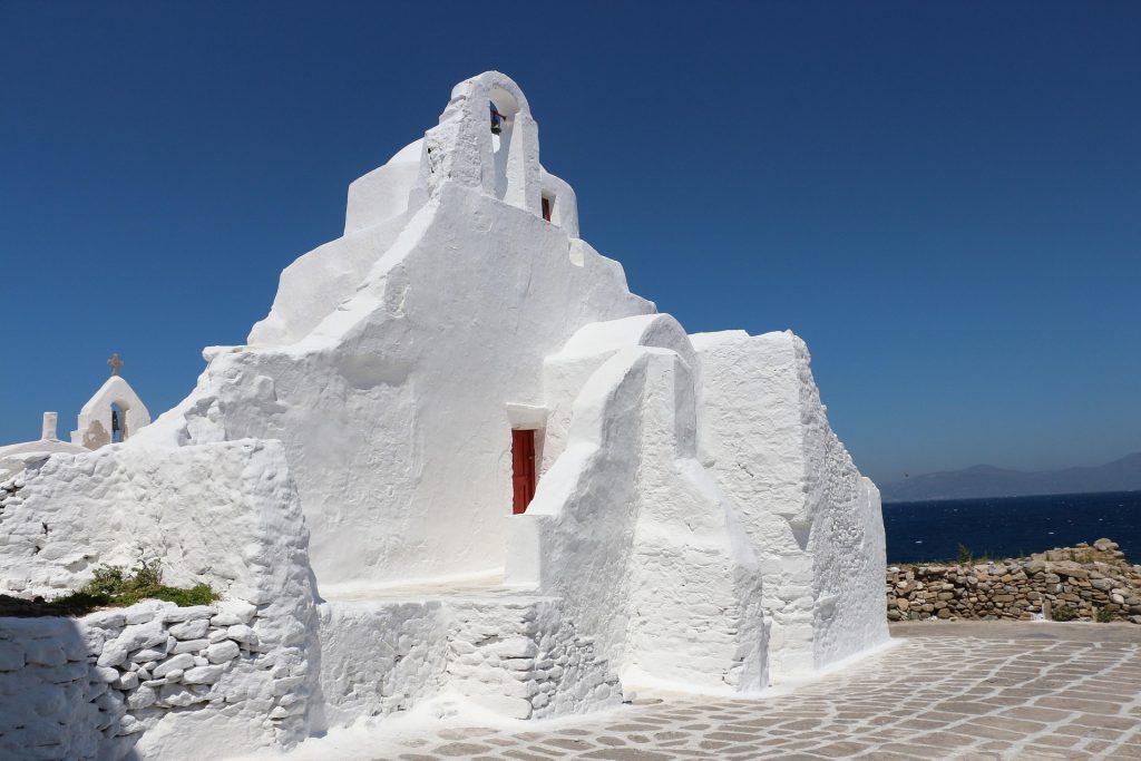Iconic whitewashed windmills with thatched roofs overlooking the blue waters of the Aegean Sea in Mykonos, Greece.
